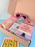 A pink gift box filled with birthday-themed items, including pink novelty sunglasses, a pink bag, a holographic bottle, a purple card, and a pink card reading 'Happy Birthday musee', with a matching 'HBD' card in front.