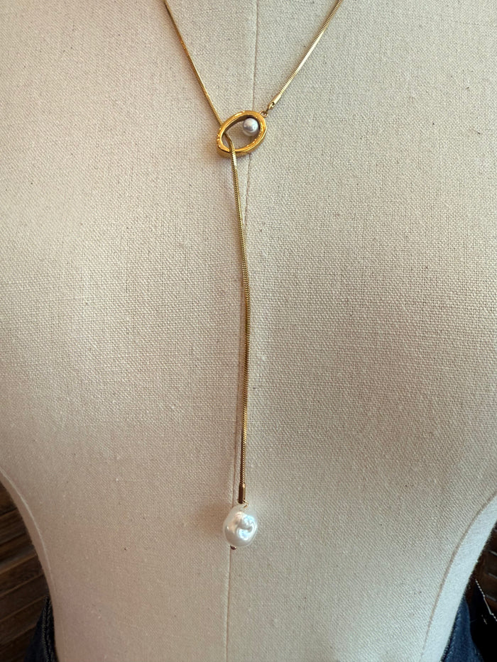 Gold round clasp lariat with dangling pearl drop, close-up on necklace front