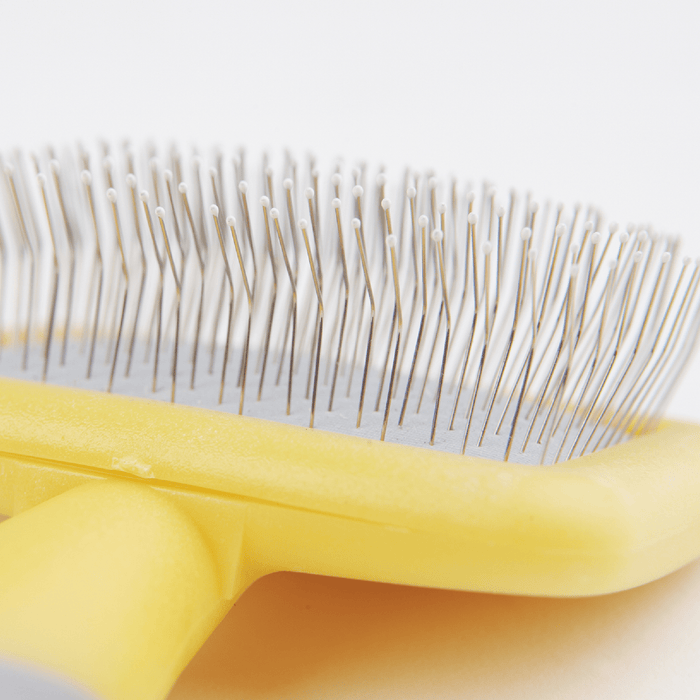White background with a close up of a  small animal Ancol yellow slicker brush with white tipped metal bristles.