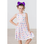 A young girl wearing a multicolored geometric pattern sleeveless knee-length dress with a higher neckline and a scoop back.