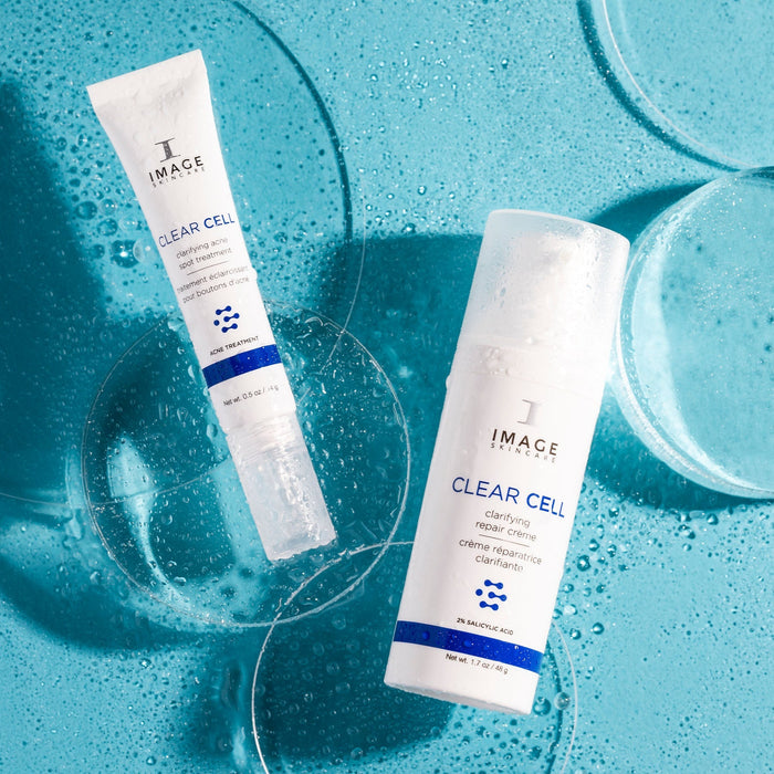 Two skincare products labeled CLEAR CELL clarifying repair crème | IMAGE Skincare displayed on a textured blue surface with water droplets and clear round glass elements.