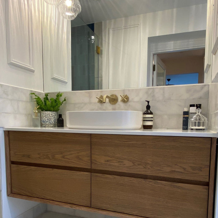 Bathroom vanity with wooden cabinets, white countertop and marble wall tiles.