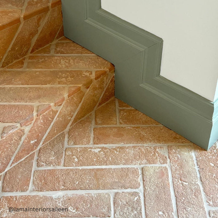 Close-up of a terracotta floor with a green skirting board and white wall.