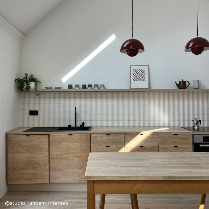 Bright kitchen with white walls, pale wood cupboards and fluted off white wall tiles.