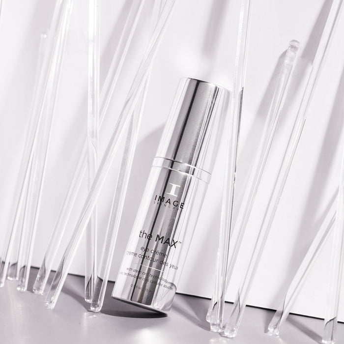Silver pump bottle of the MAX™ eye crème | IMAGE Skincare standing among clear acrylic rods on a reflective surface in soft lighting for skincare and wellness promotion.